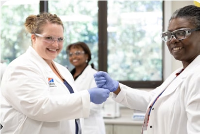 Tre donne sorridenti, scienziate in camice bianco e occhiali protettivi