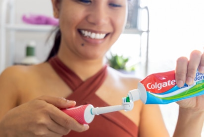 Una donna sorride mentre mette il dentifricio Colgate su uno spazzolino da denti in un bagno.